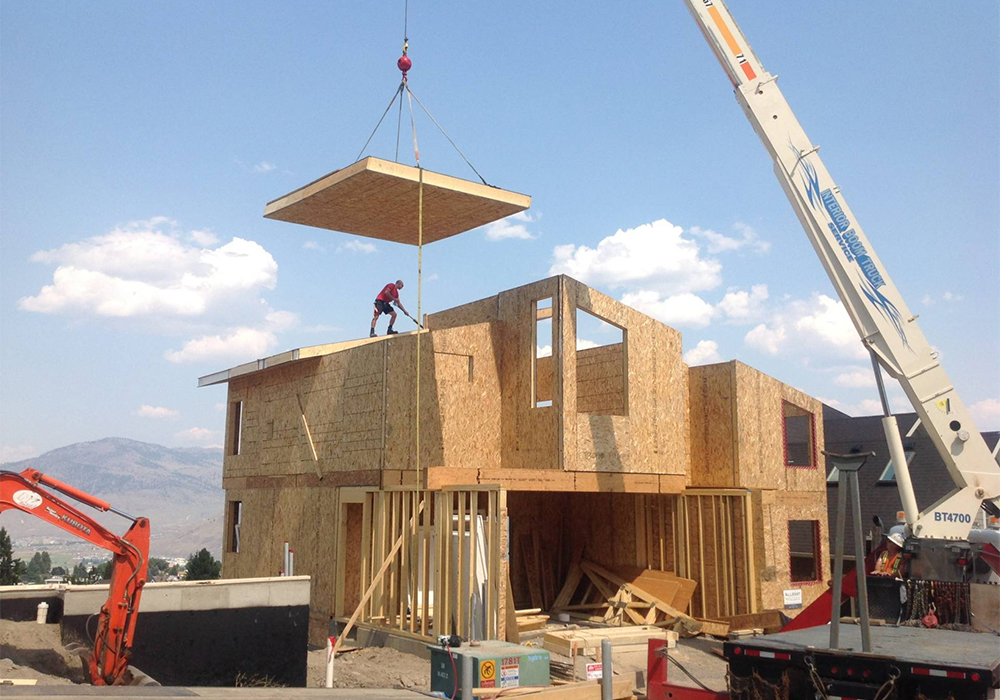 A crane lowering a roof panel onto an under construction home