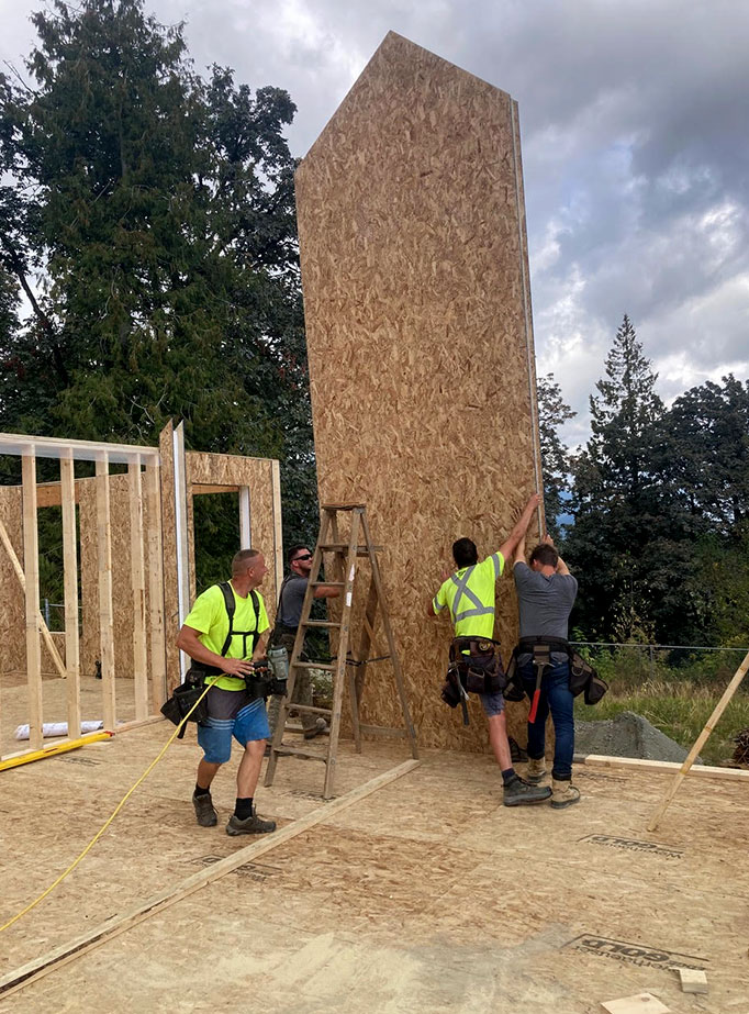 Construction workers lifting a plywood wall panel for a house under construction