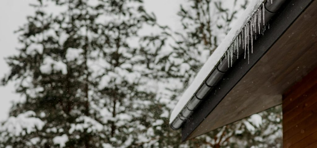 Snow on a home's roof with icicles hanging from the gutter