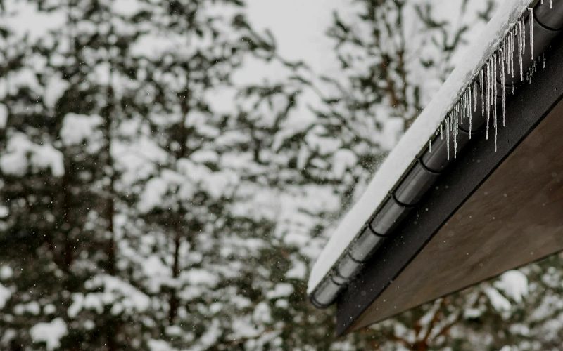 Snow on a home's roof with icicles hanging from the gutter